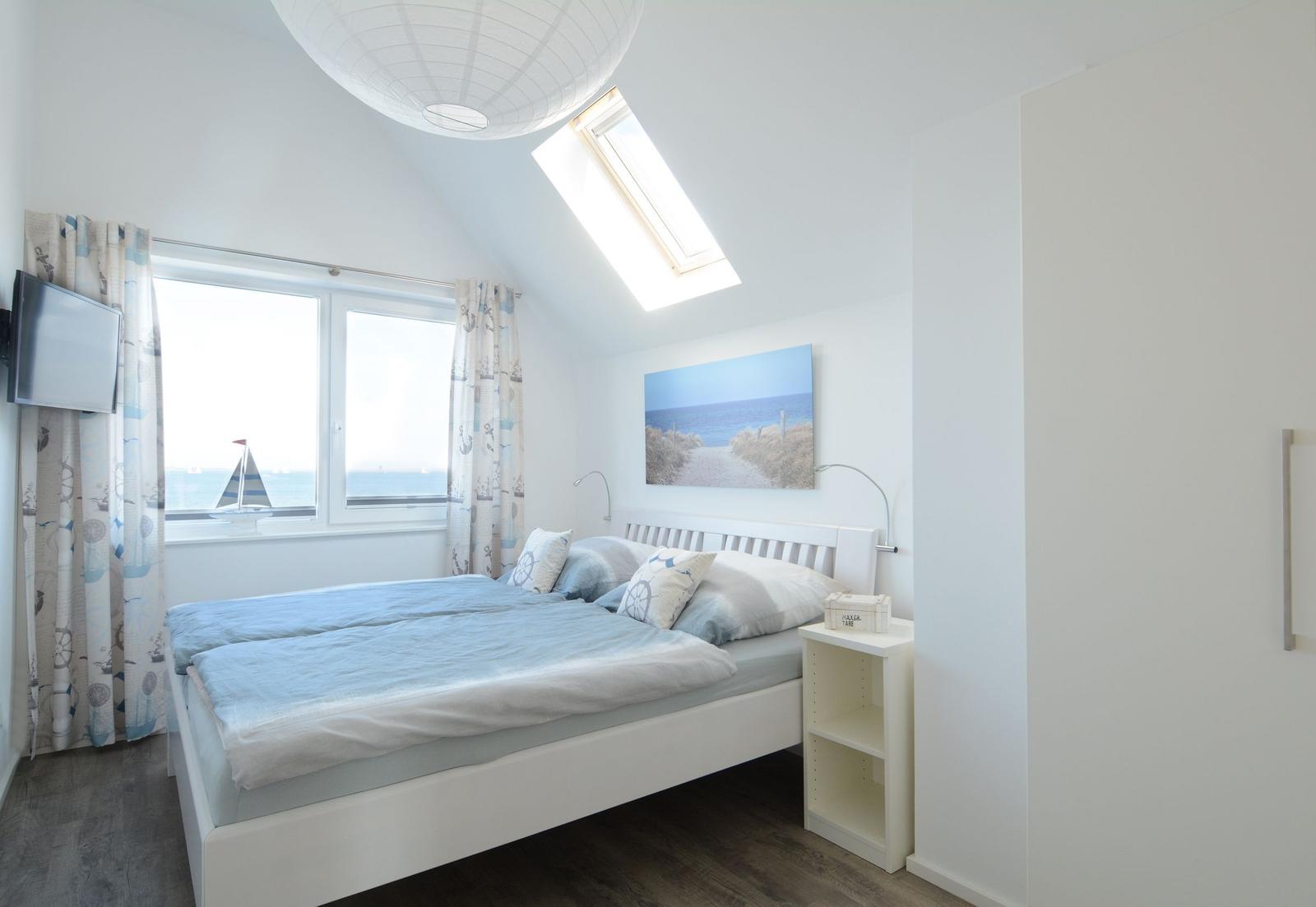 Schlafzimmer mit Blick aufs Meer, Bett, Nachttisch und Dachfenster.