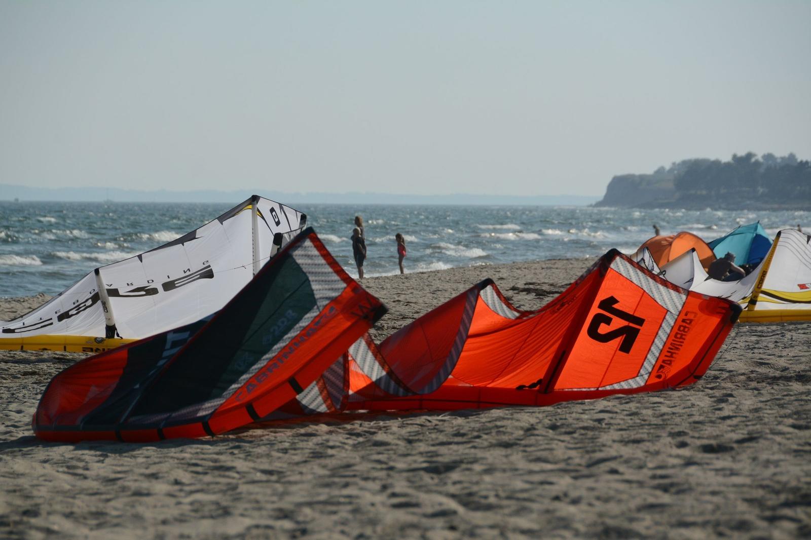 Kites liegen am Strand, Menschen im Wasser, Blick aufs Meer.