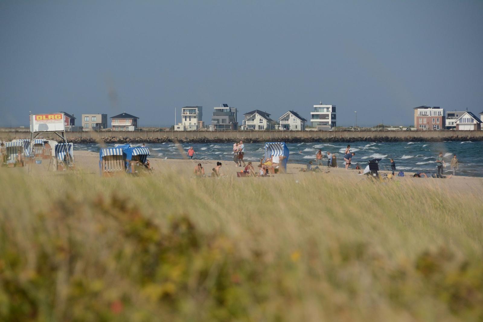 Strand mit Strandkörben und Wellen. Im Hintergrund stehen Häuser am Ufer.