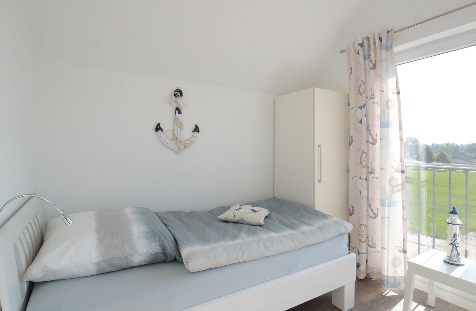 Schlafzimmer mit Bett, Garderobe und Blick auf Balkon.