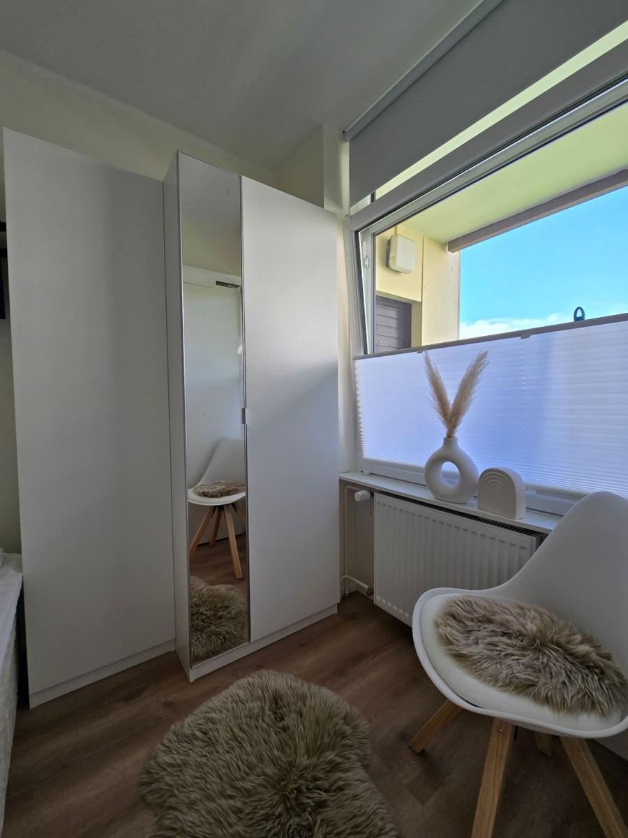 Schlafzimmer mit Kleiderschrank, Stuhl und Fenster mit Jalousie.