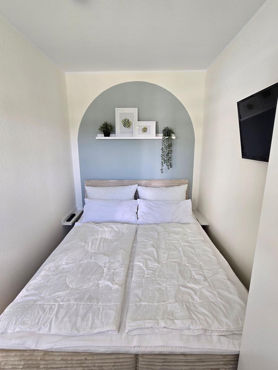 Schlafzimmer mit Doppelbett, Wandregal und Fernseher.