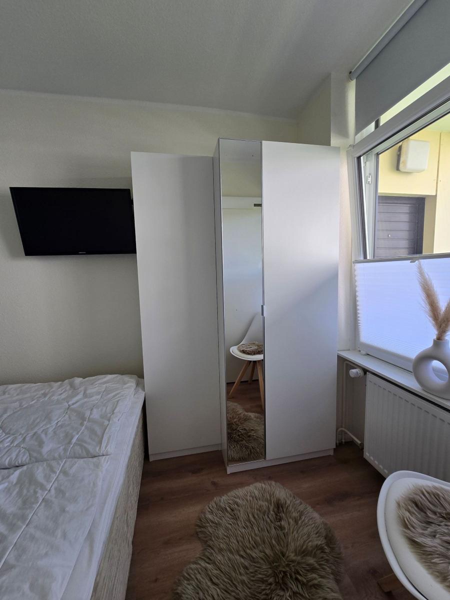 Schlafzimmer mit Bett, Kleiderschrank und TV. Fenster mit Jalousie.