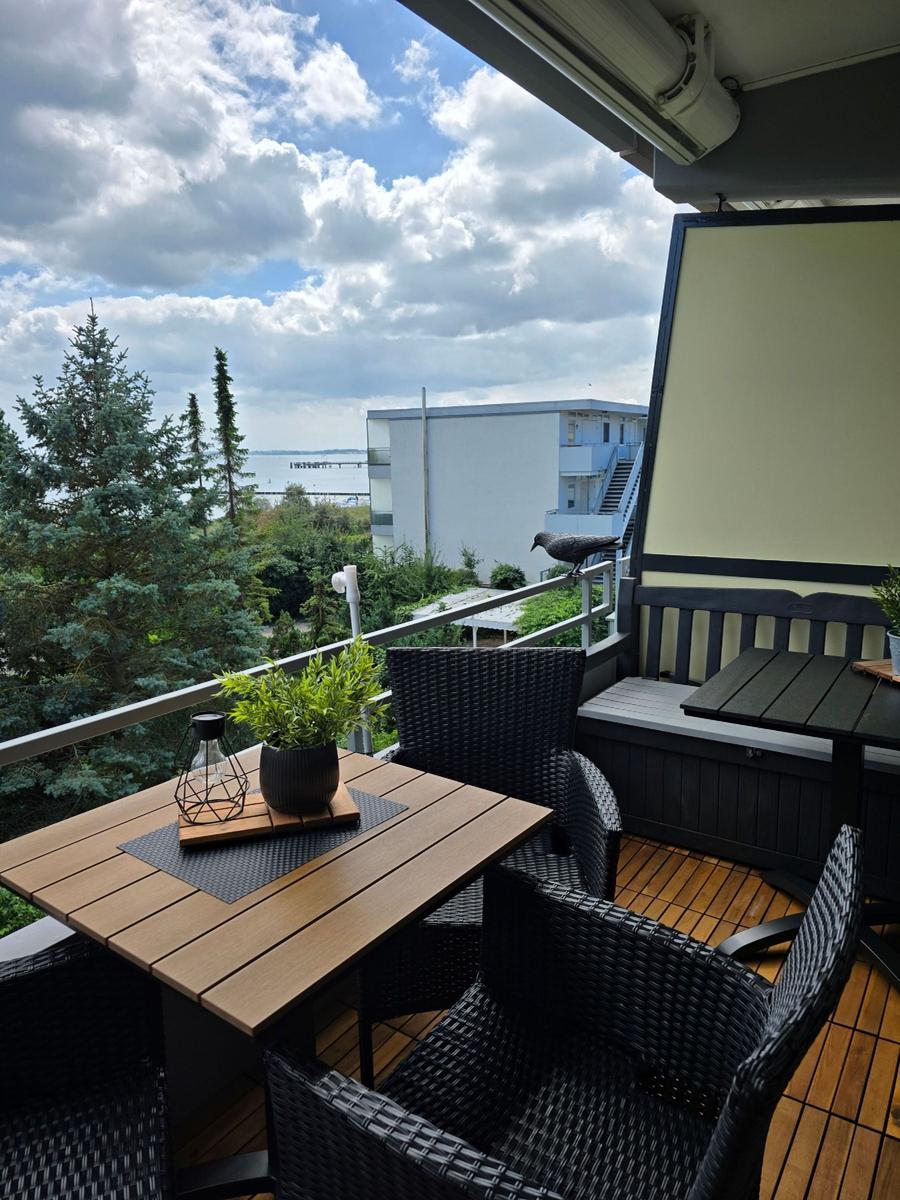 Terrasse mit Tisch, Stühlen und Blick auf Wasser und Bäume.