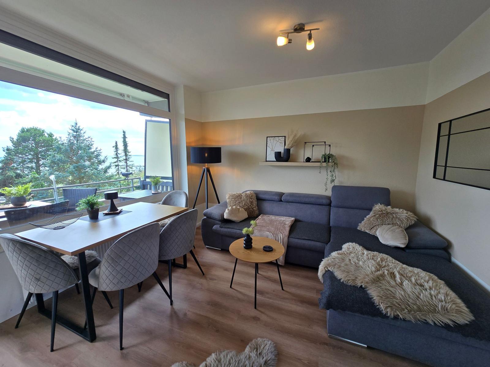 Wohn- und Essbereich mit Balkonblick. Sofa, Tisch und Stühle.