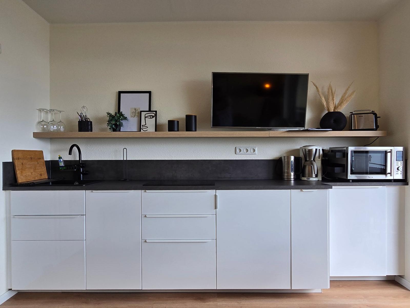 Küche mit weißen Schränken, schwarzer Arbeitsplatte und integriertem Fernseher.