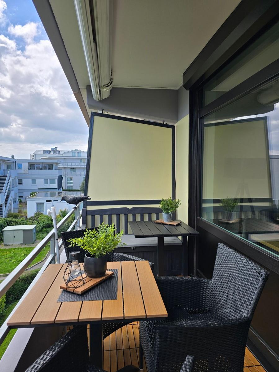 Terrasse mit Tisch, Stühlen und Pflanzen. Blick auf Wohngebiet mit Gebäuden.
