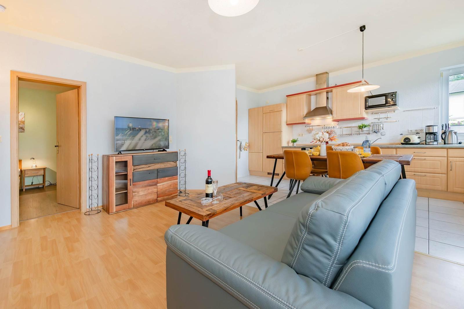 Wohnzimmer mit Sofa, TV und Küchenbereich mit Esstisch.