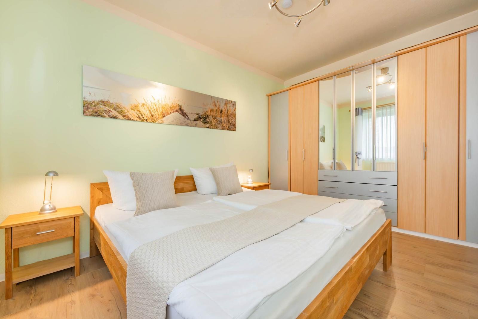 Schlafzimmer mit Doppelbett, Kleiderschrank und Wandbild.