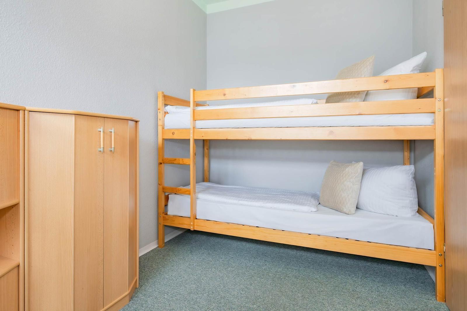 Zimmer mit Doppelstockbett und Holzschrank.