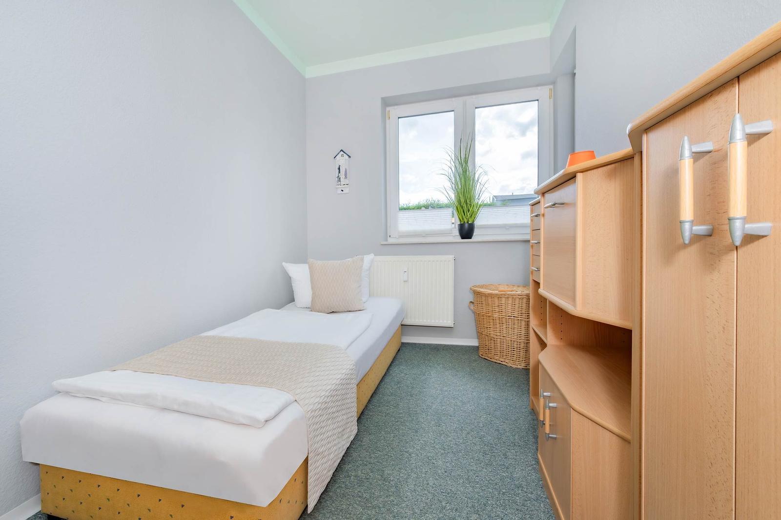 Ein Schlafzimmer mit Einzelbett, Holzschrank und Fenster mit Pflanze.