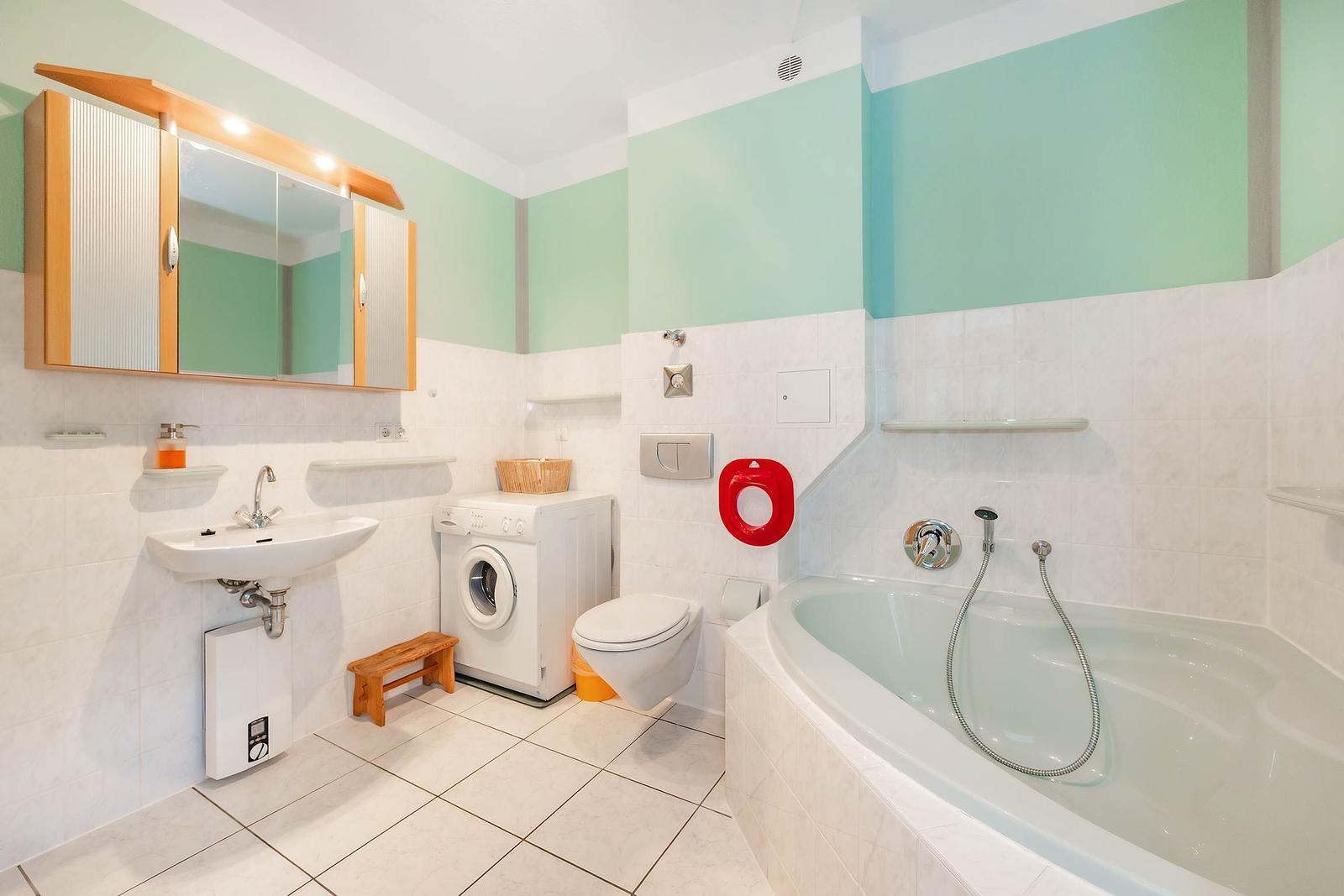 Badezimmer mit Badewanne, Waschmaschine und Spiegelkabinett.