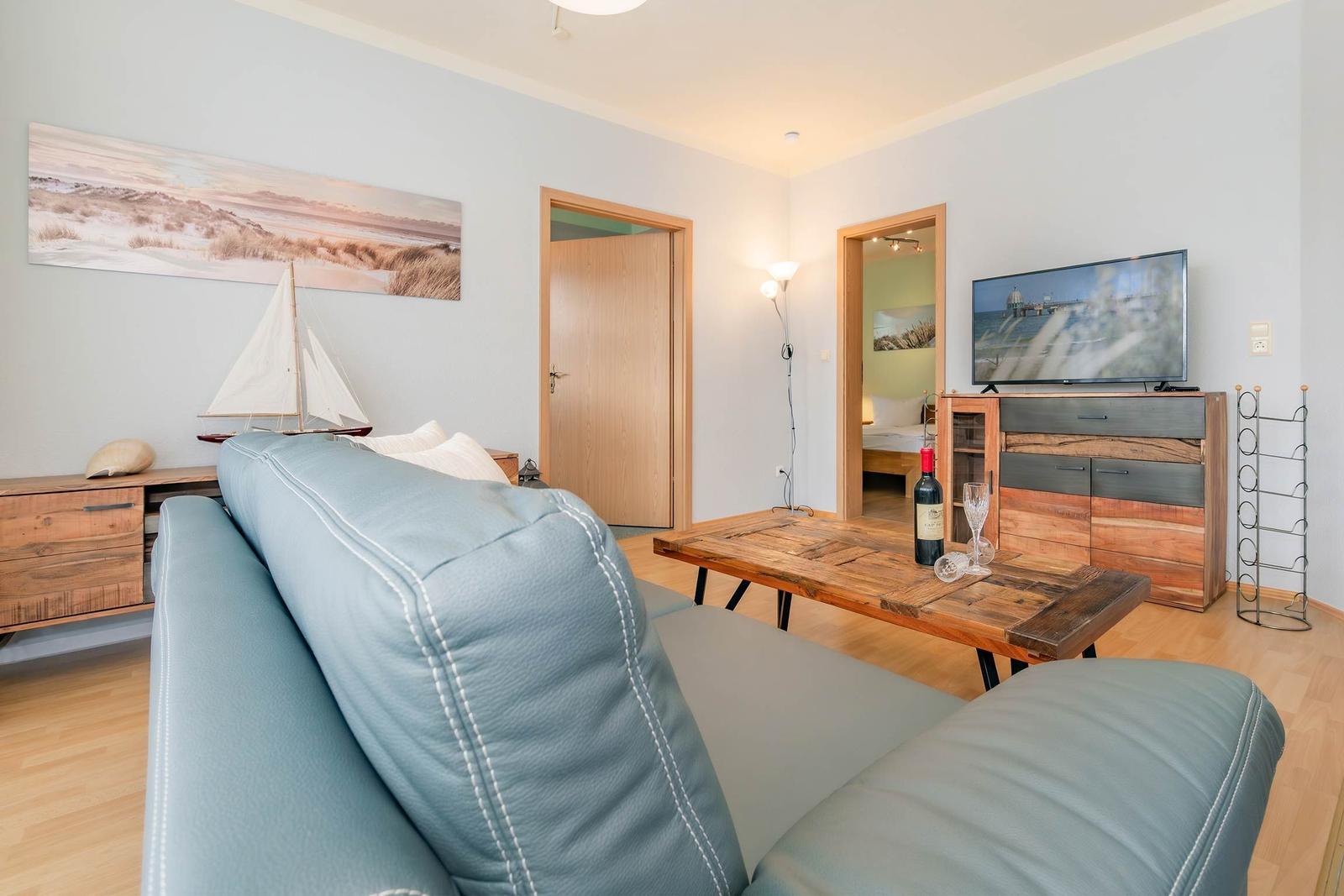 Wohnzimmer mit Sofa, Tisch, Fernseher und Blick in Schlafzimmer.