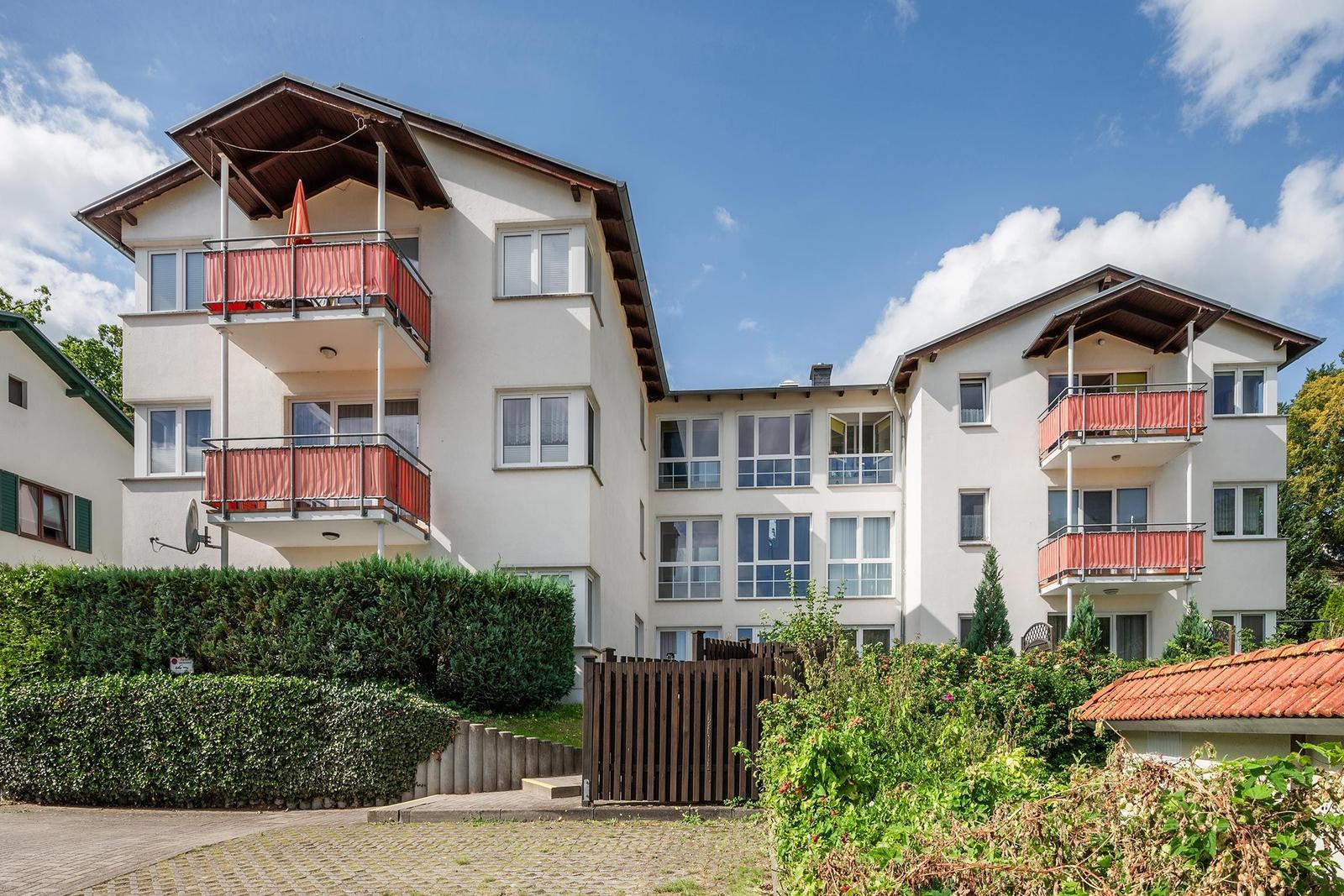 Wohnhaus mit Balkonen und grüner Umgebung unter blauem Himmel.
