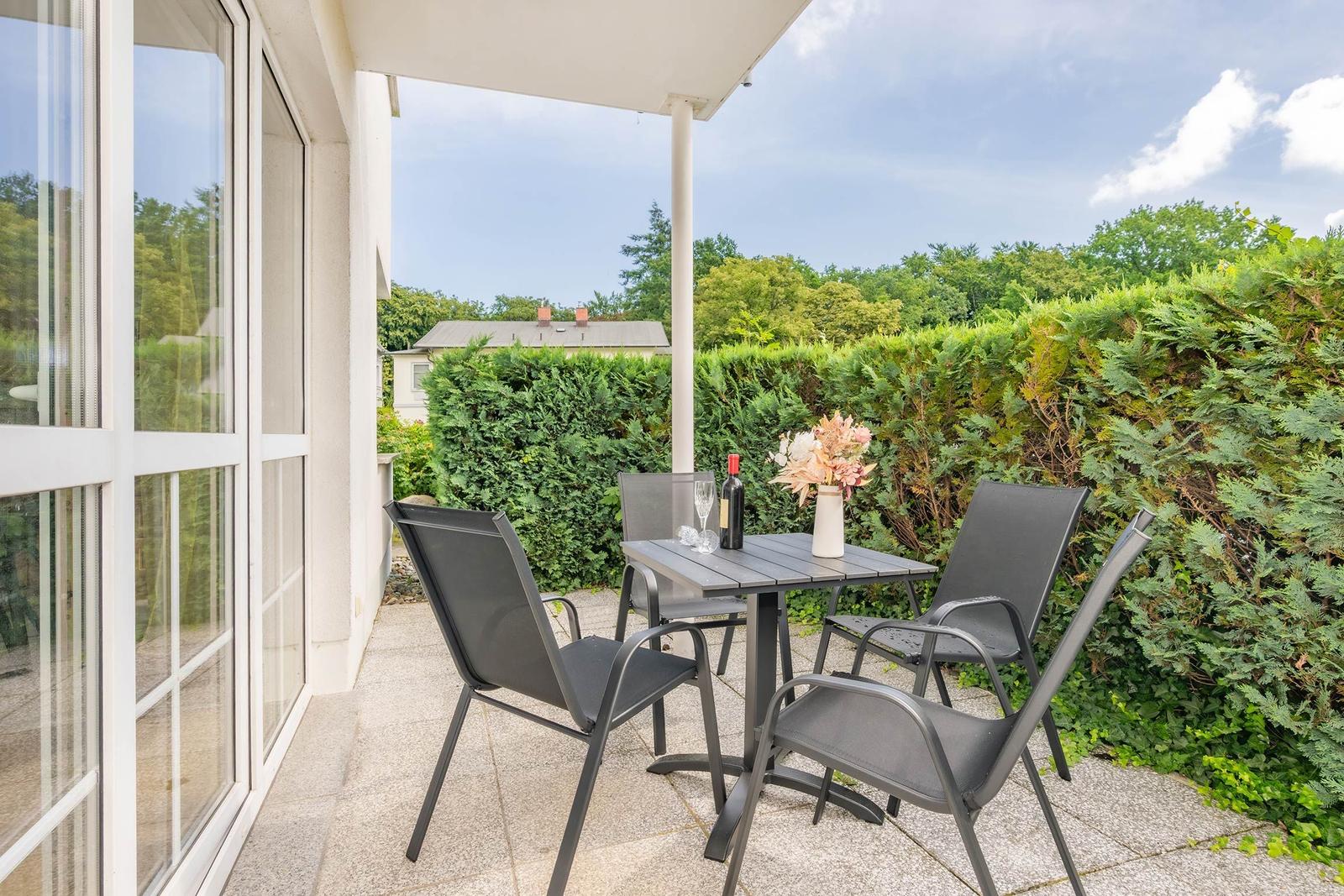 Terrasse mit Tisch und Stühlen, umgeben von grünen Hecken.