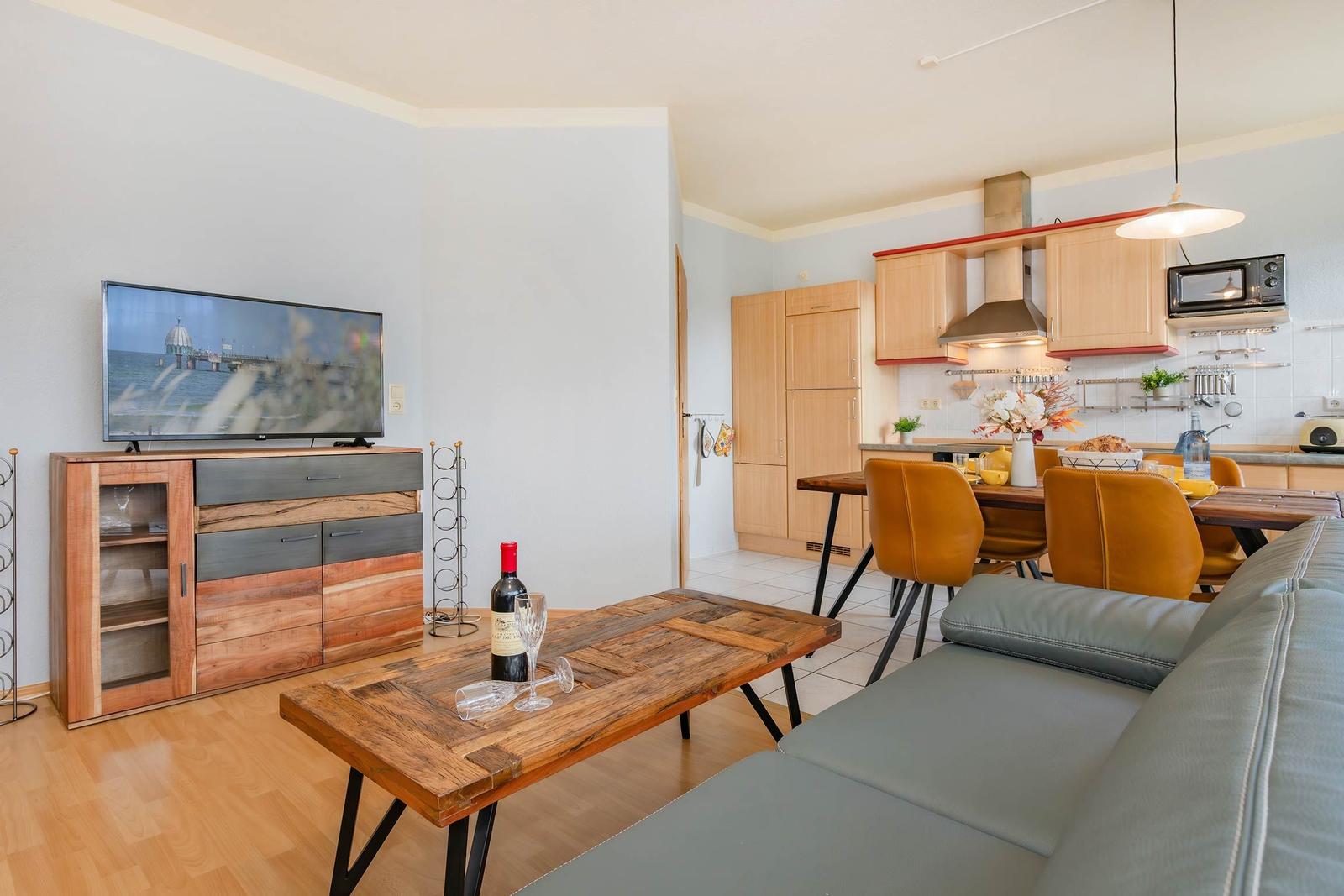 Wohnzimmer mit Küchenbereich, Couch, Tisch und TV.