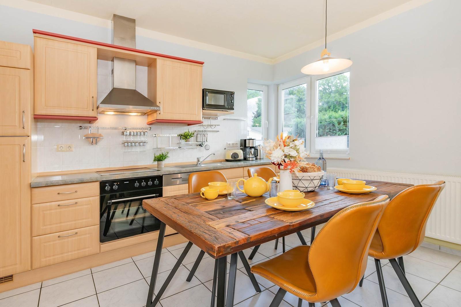 Küche mit Essbereich, Holztisch und gelben Stühlen. Fenster mit Blick auf Grün.