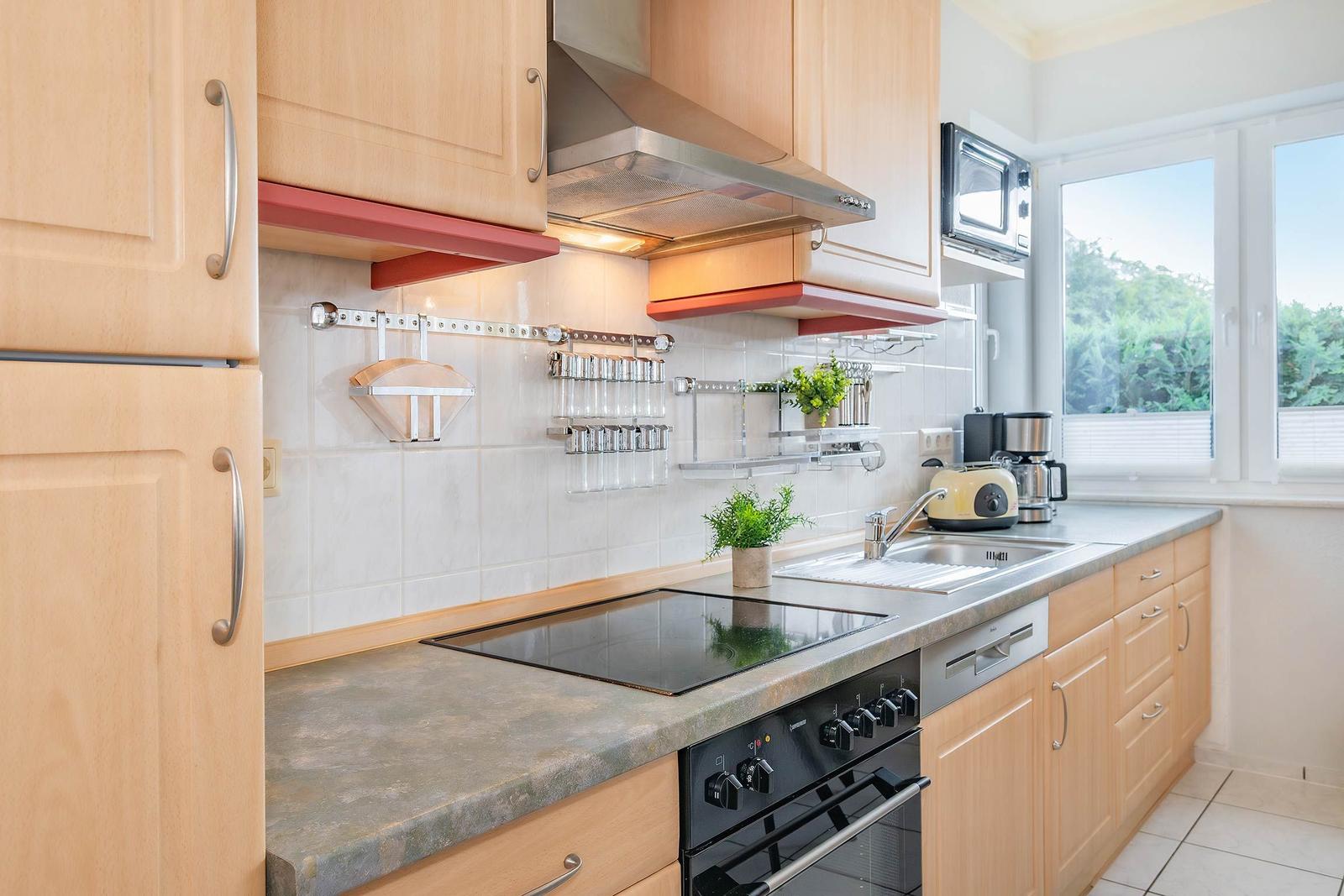 Küche mit Holzschränken, Herd, Spüle und Fenster mit Blick auf Grün.