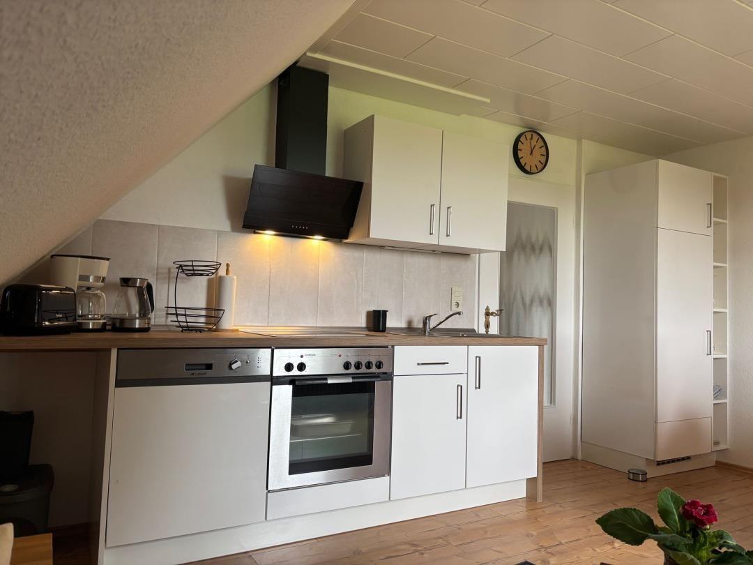 Küche mit weißen Schränken, Edelstahlgeräten und Holzoberfläche.