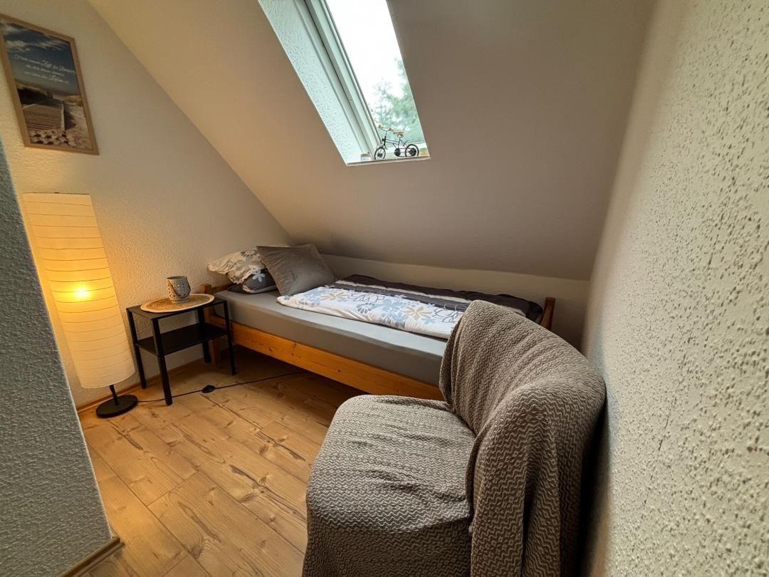 Dachgeschosszimmer mit Bett, Sessel und Dachfenster.