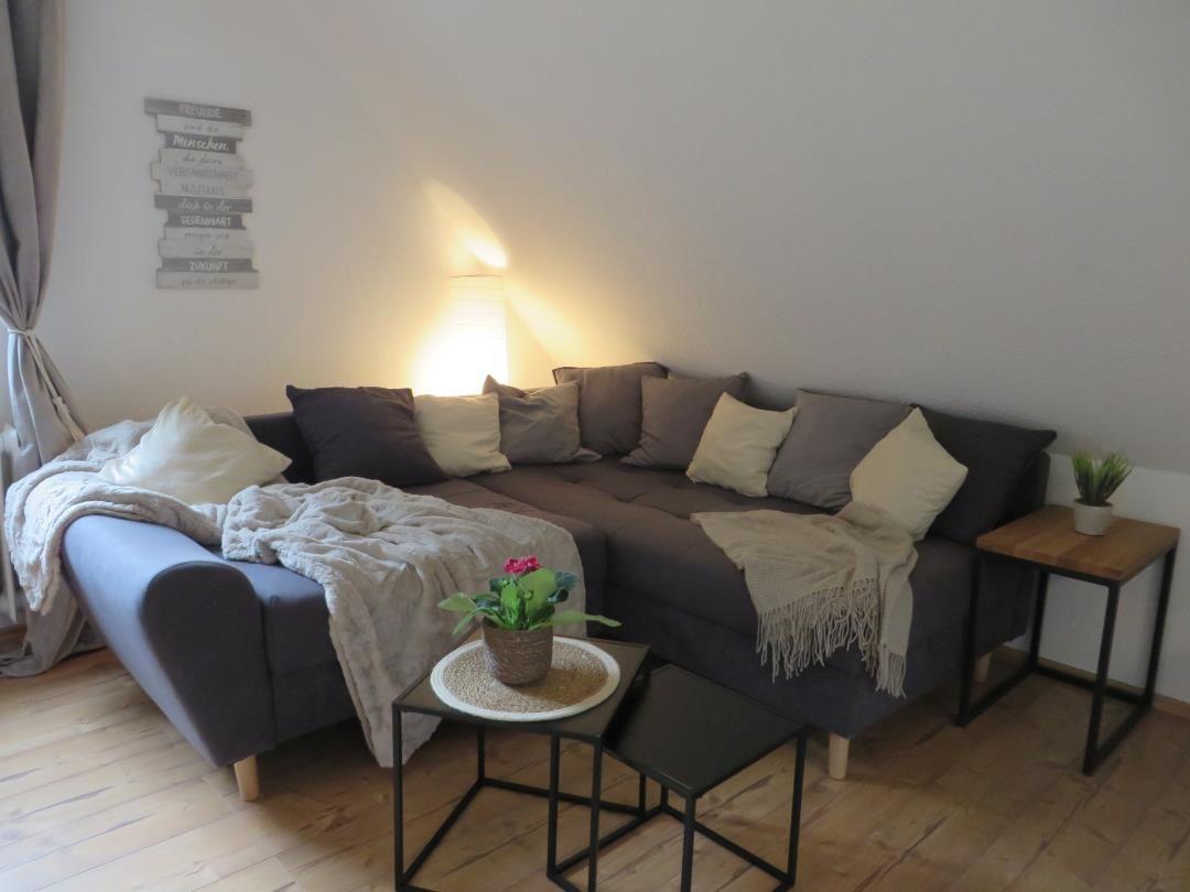 Ein Wohnzimmer mit Ecksofa, Beistelltischen und Pflanzen.