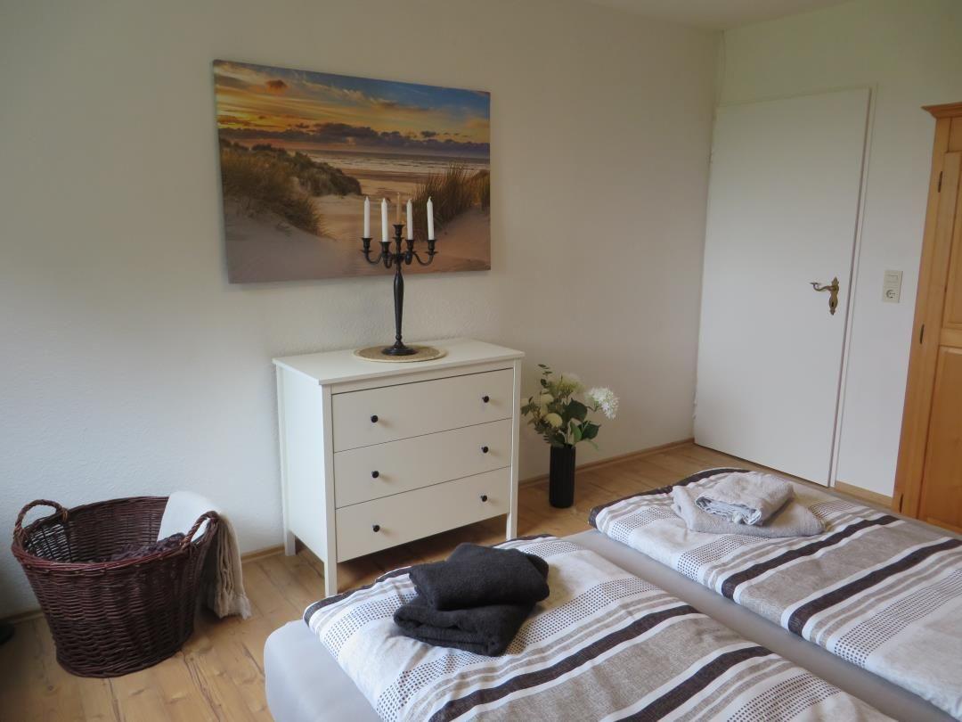 Zimmer mit Bett, Schrank, Bild und Blumen.