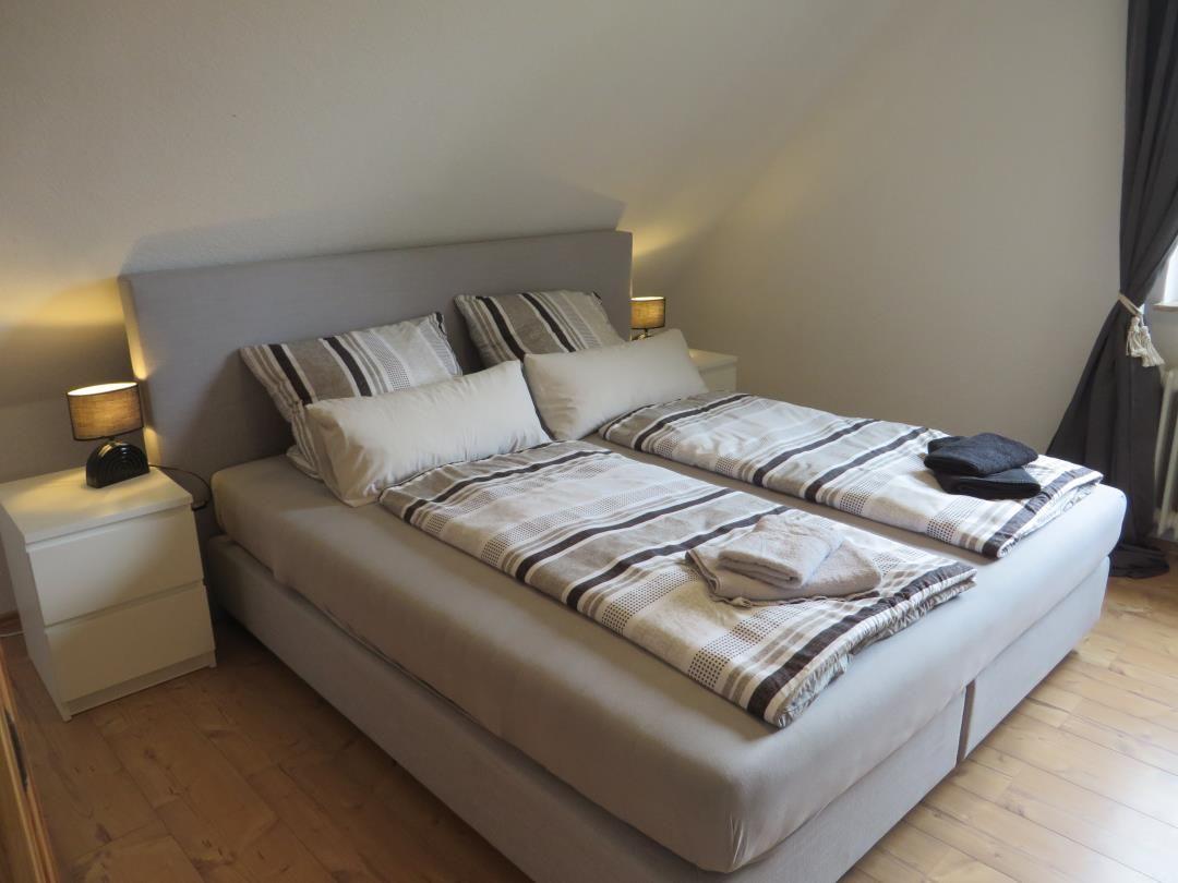 Doppelbett mit Bettwäsche, zwei Nachttische und Lampen.