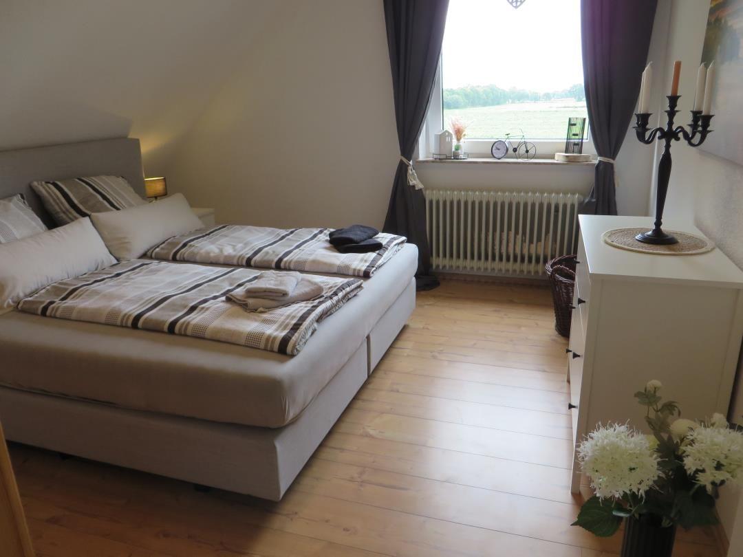 Schlafzimmer mit Doppelbett, Holzboden und Fenster mit Blick auf Feld.