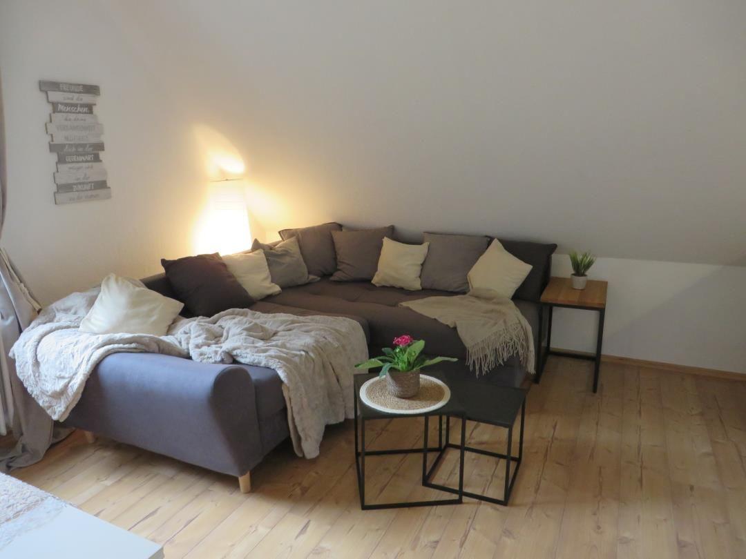 Wohnzimmer mit Ecksofa, Beistelltisch und Pflanzen auf Holzboden.