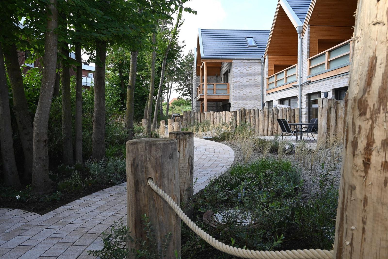 Pflasterweg durch Grünanlagen zu modernen Häusern mit Balkonen.