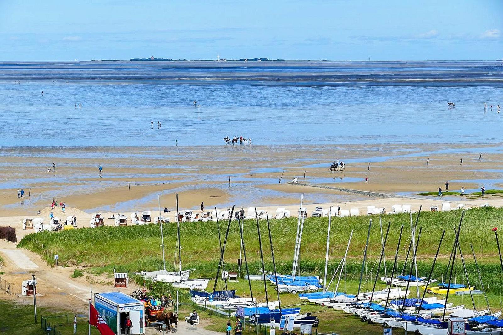 Strand mit Wattgebieten, Segelboote und Strandkörben. Menschen genießen das Wasser.