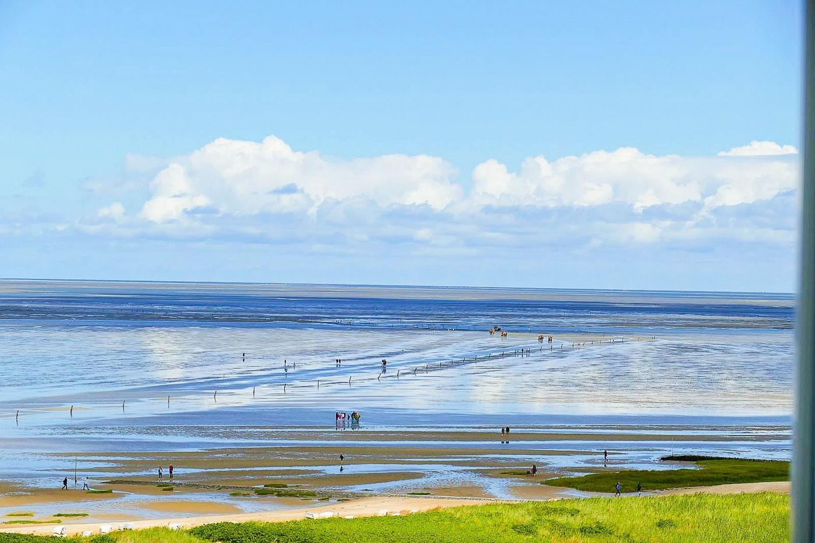 Weitläufiger Strand mit Wattgebieten und wenigen Personen unter blauem Himmel.