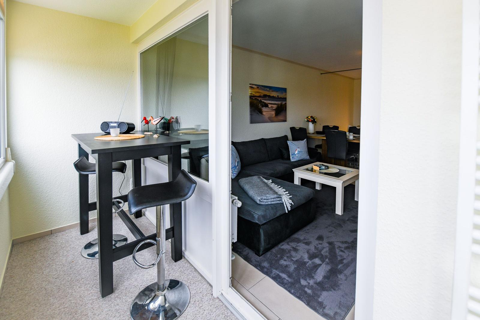 Barhocker und Tisch im Vordergrund. Wohnzimmer mit Sofa und Couchtisch im Hintergrund.