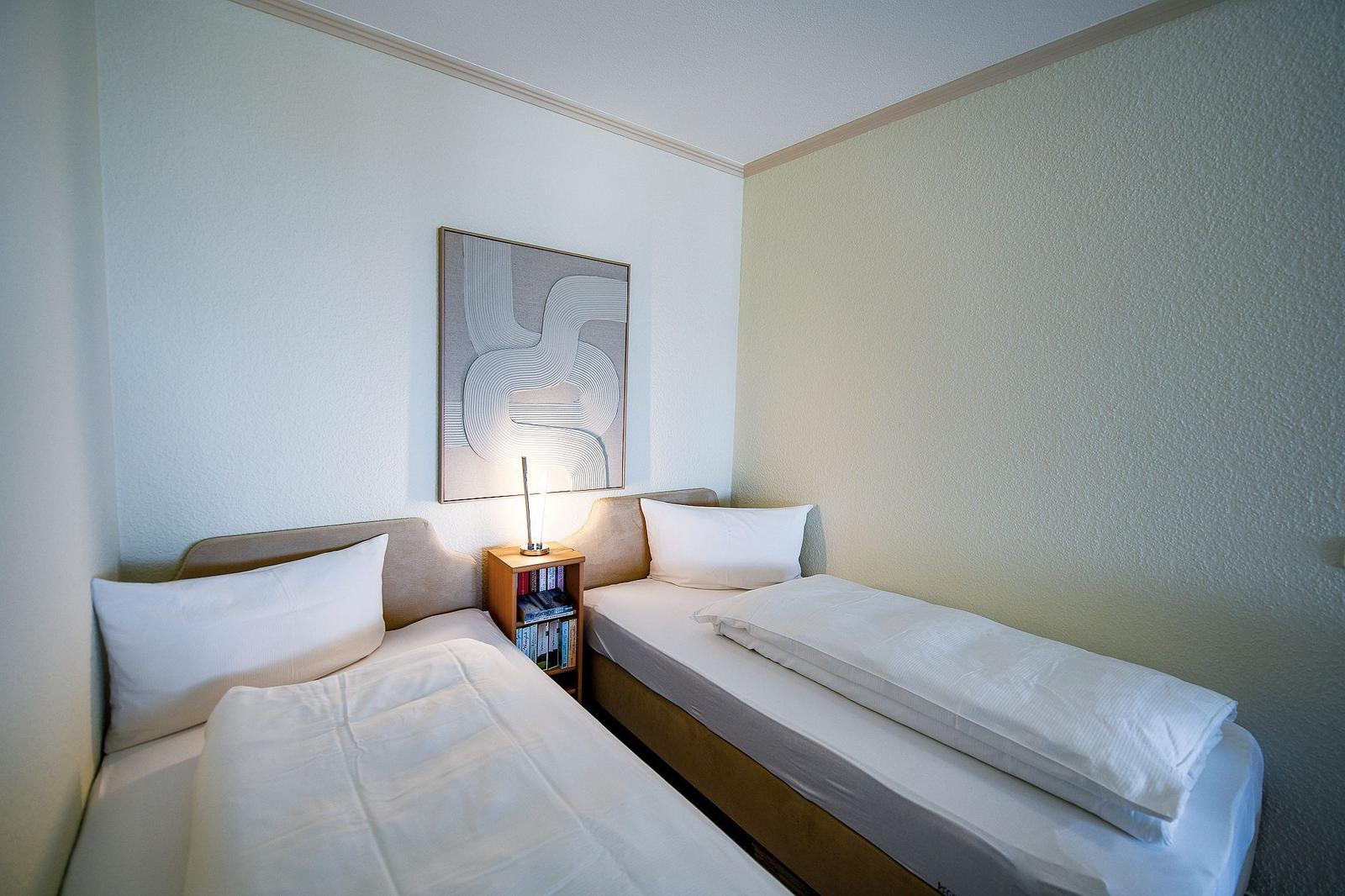 Zwei Einzelbetten mit weißen Bettwäschen und einem Nachttisch mit Lampe.