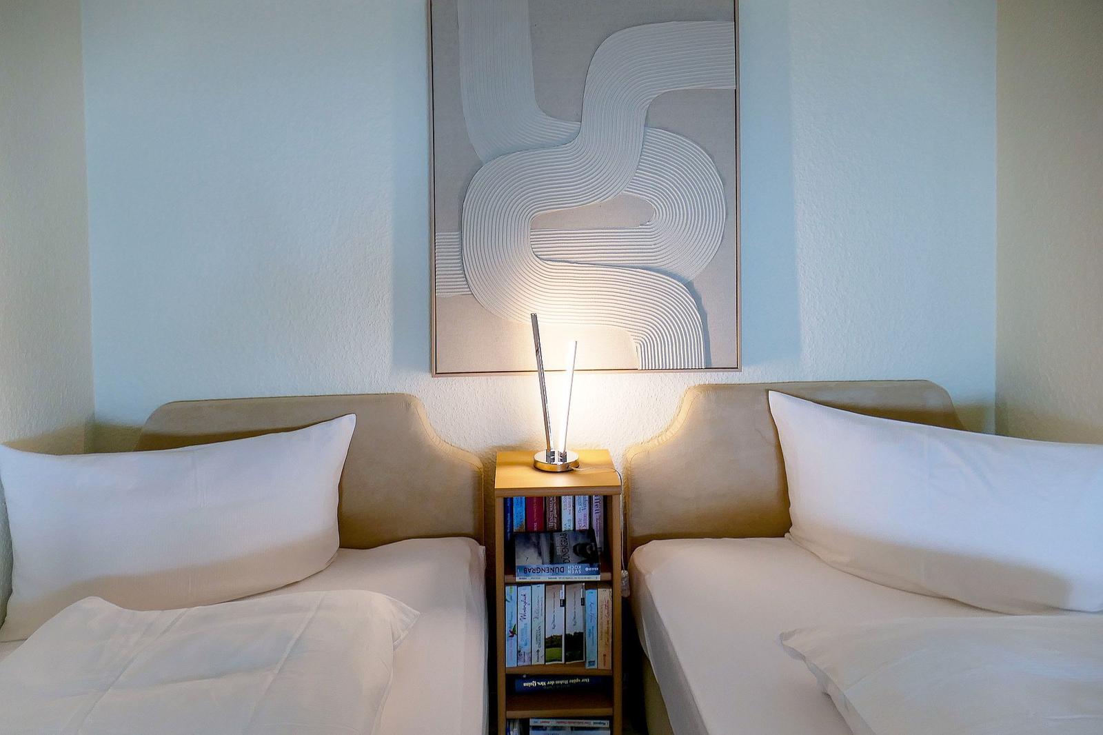 Zwei Betten mit weißen Kissen und einer Nachttischlampe zwischen ihnen.