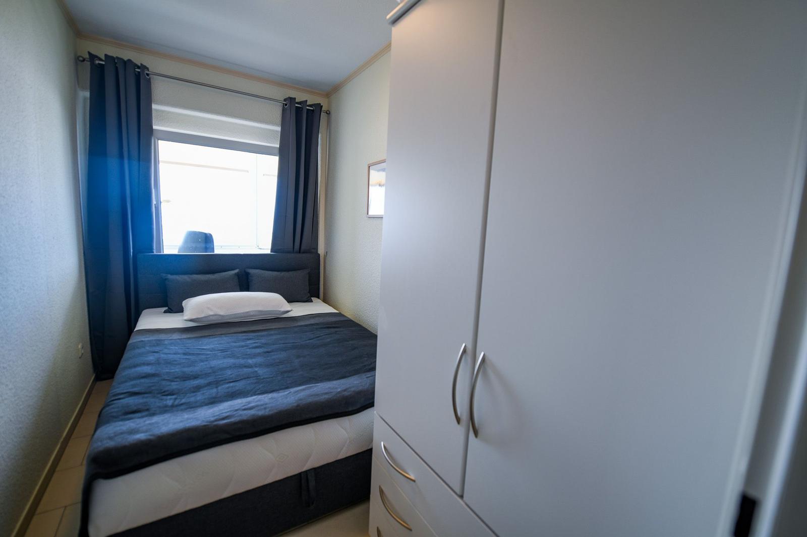 Schlafzimmer mit Bett, Gardinen und Kleiderschrank.