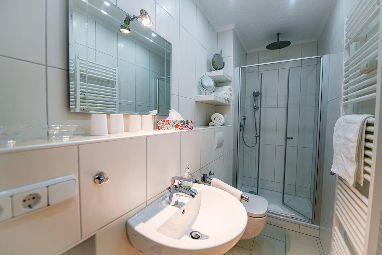 Badezimmer mit Dusche, Waschbecken und Heizkörper.