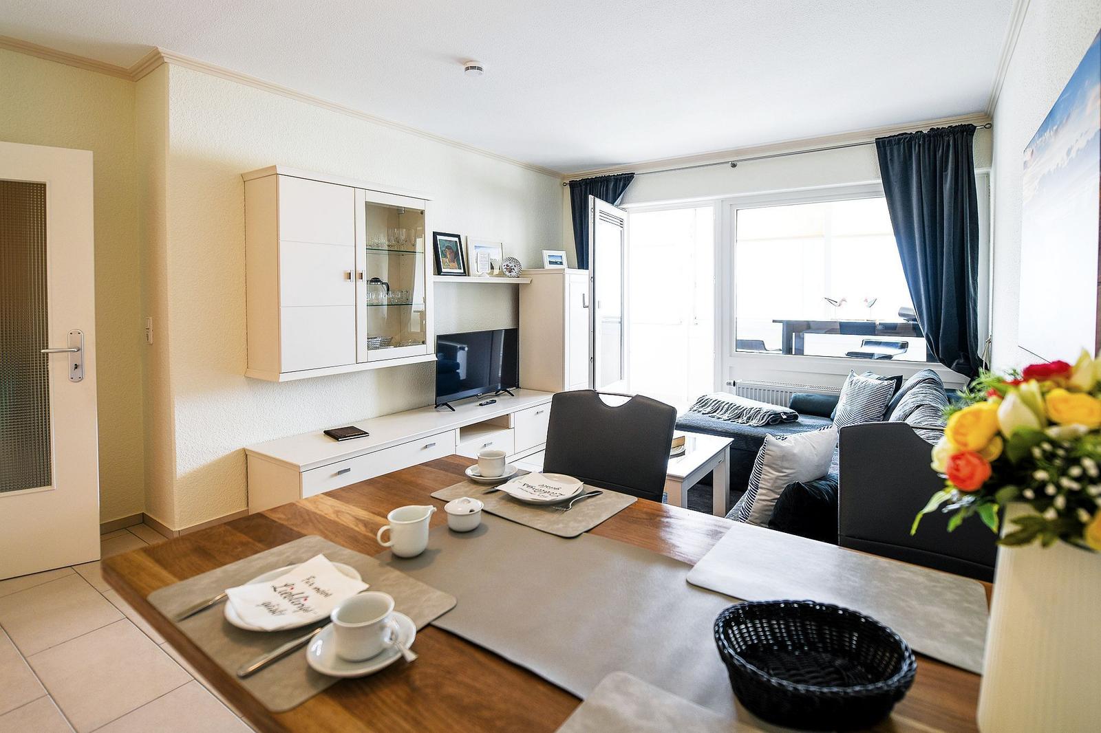 Essbereich mit Tisch, Stühlen und Blick auf Wohnzimmer mit Sofa und TV.