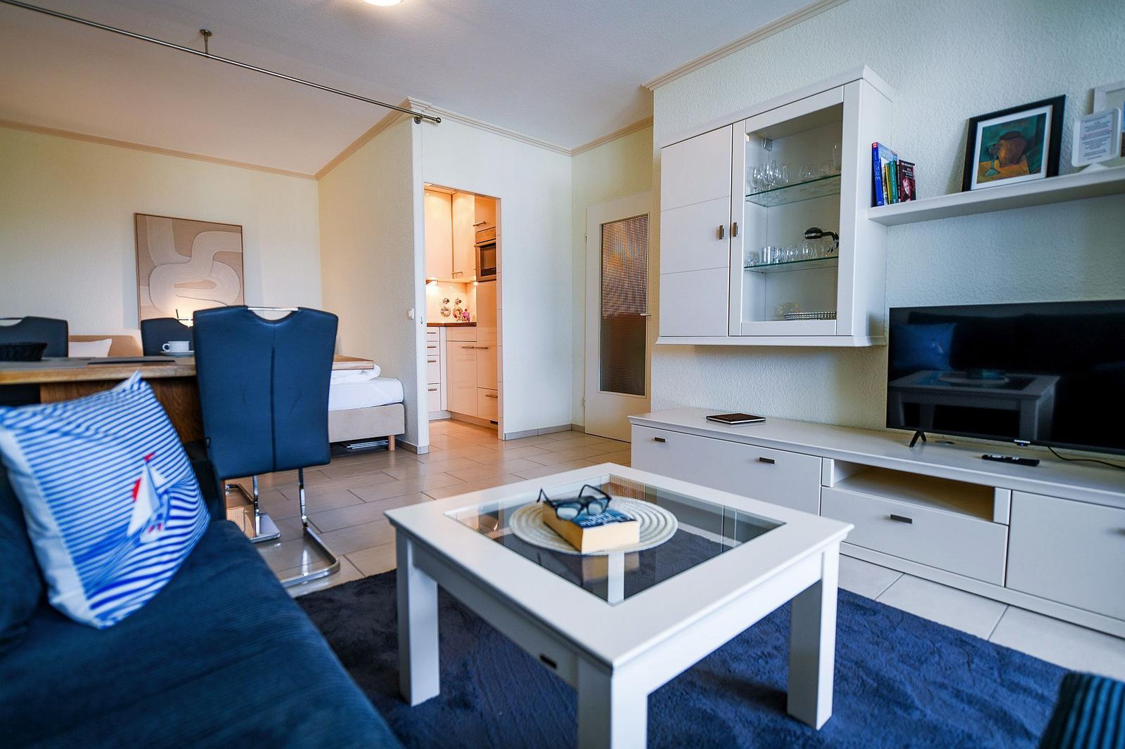 Wohnbereich mit Sofa, Couchtisch und TV. Küche und Schlafzimmer sind sichtbar.