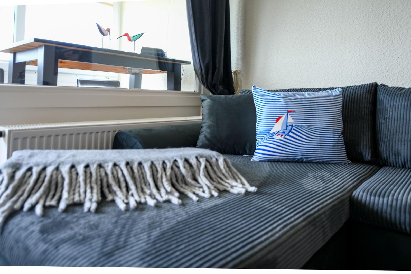 Ein Sofa mit Kissen und Decke vor einem Fenster mit Tisch und Vögeln.