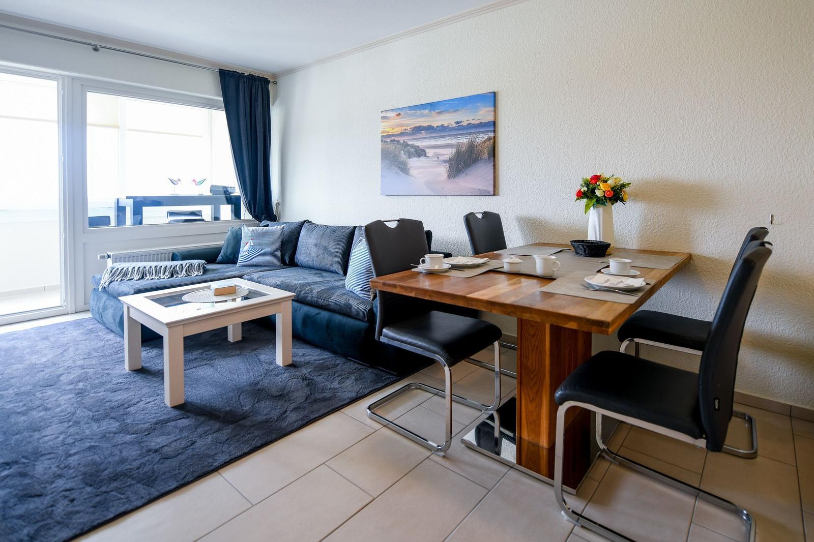 Wohn- und Essbereich mit Sofa, Tisch und Stühlen. Wandbild und Blumen.