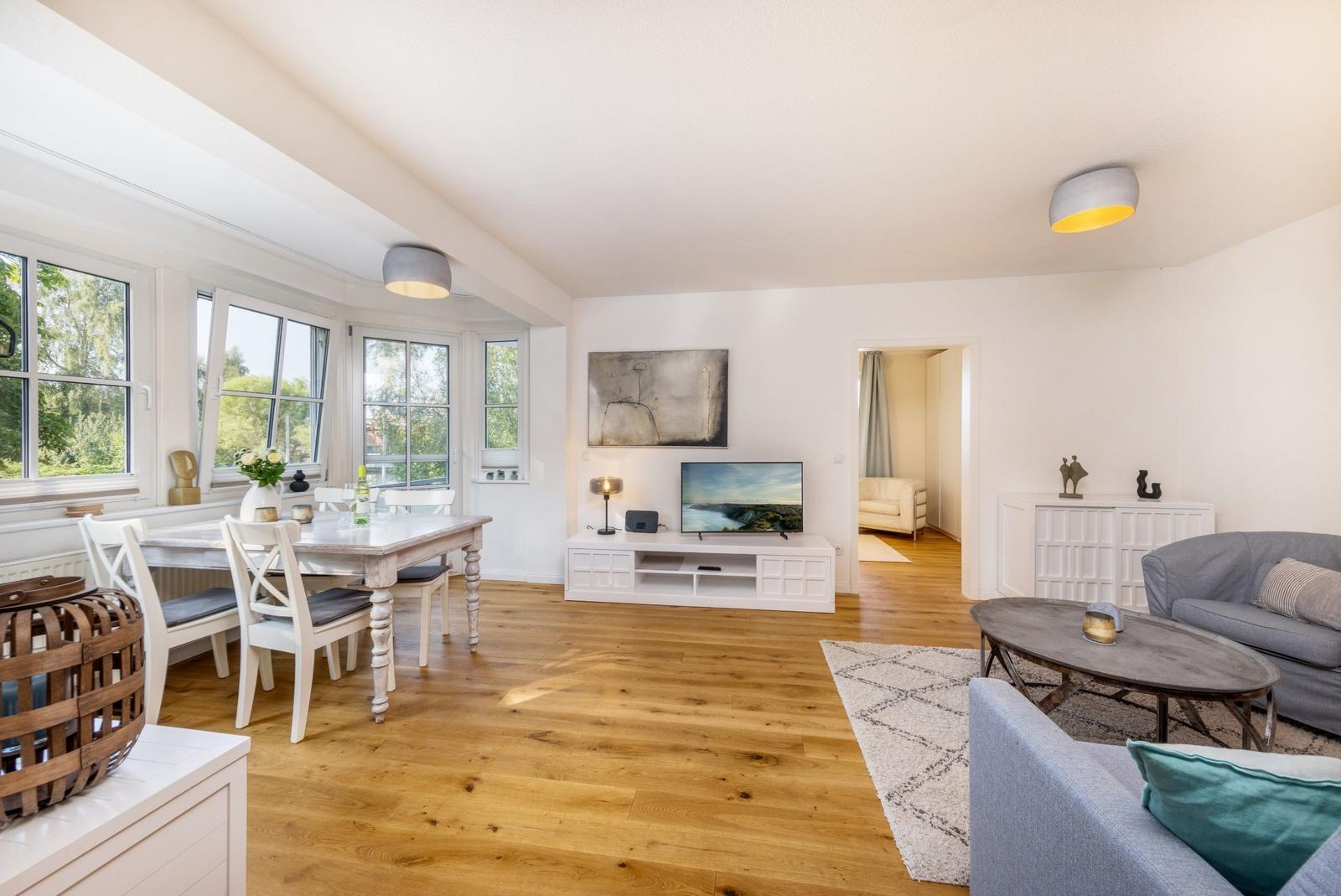 Wohn- und Essbereich mit Holzboden, TV, Sofa und Fenstern.