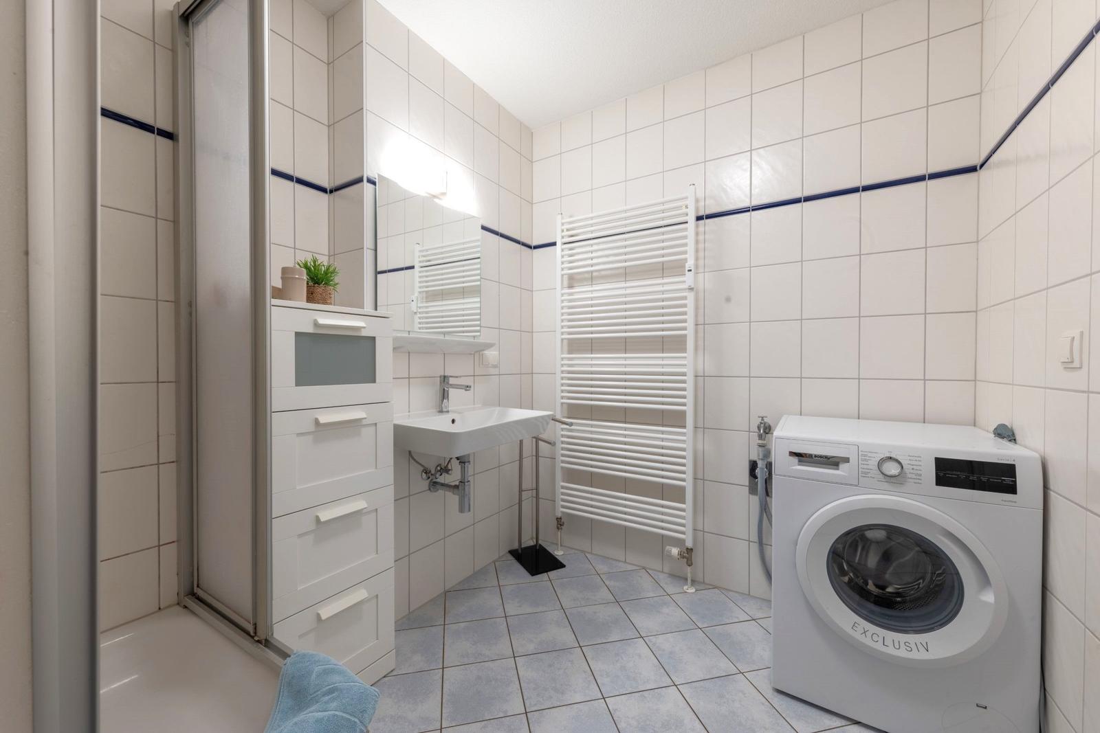 Badezimmer mit Waschmaschine, Handwaschbecken und Dusche.