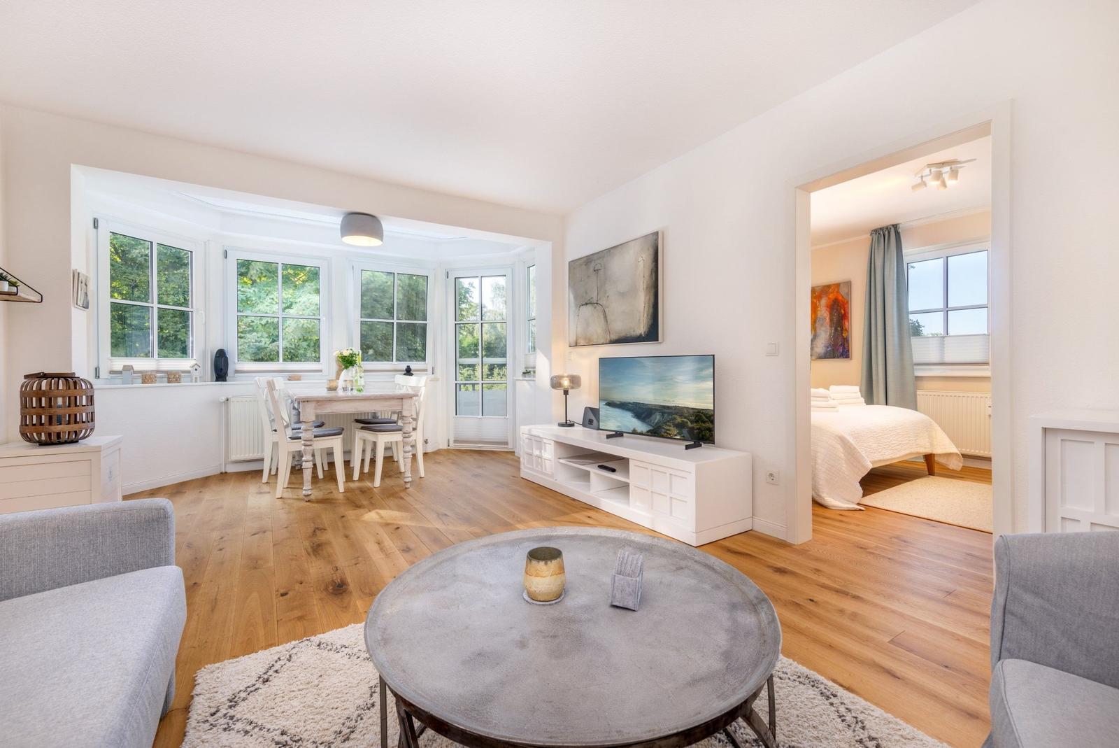 Wohn- und Essbereich mit Holzboden und TV. Schlafzimmer mit Bett und Fenster sichtbar.