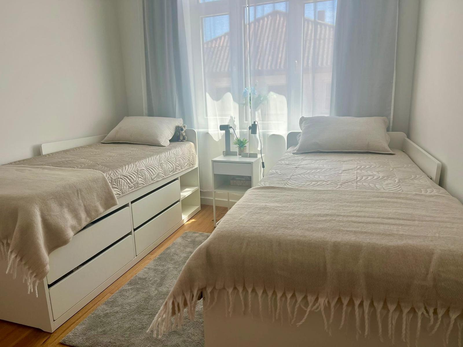 Zwei Betten mit hellen Bezügen und einem Nachttisch zwischen ihnen.