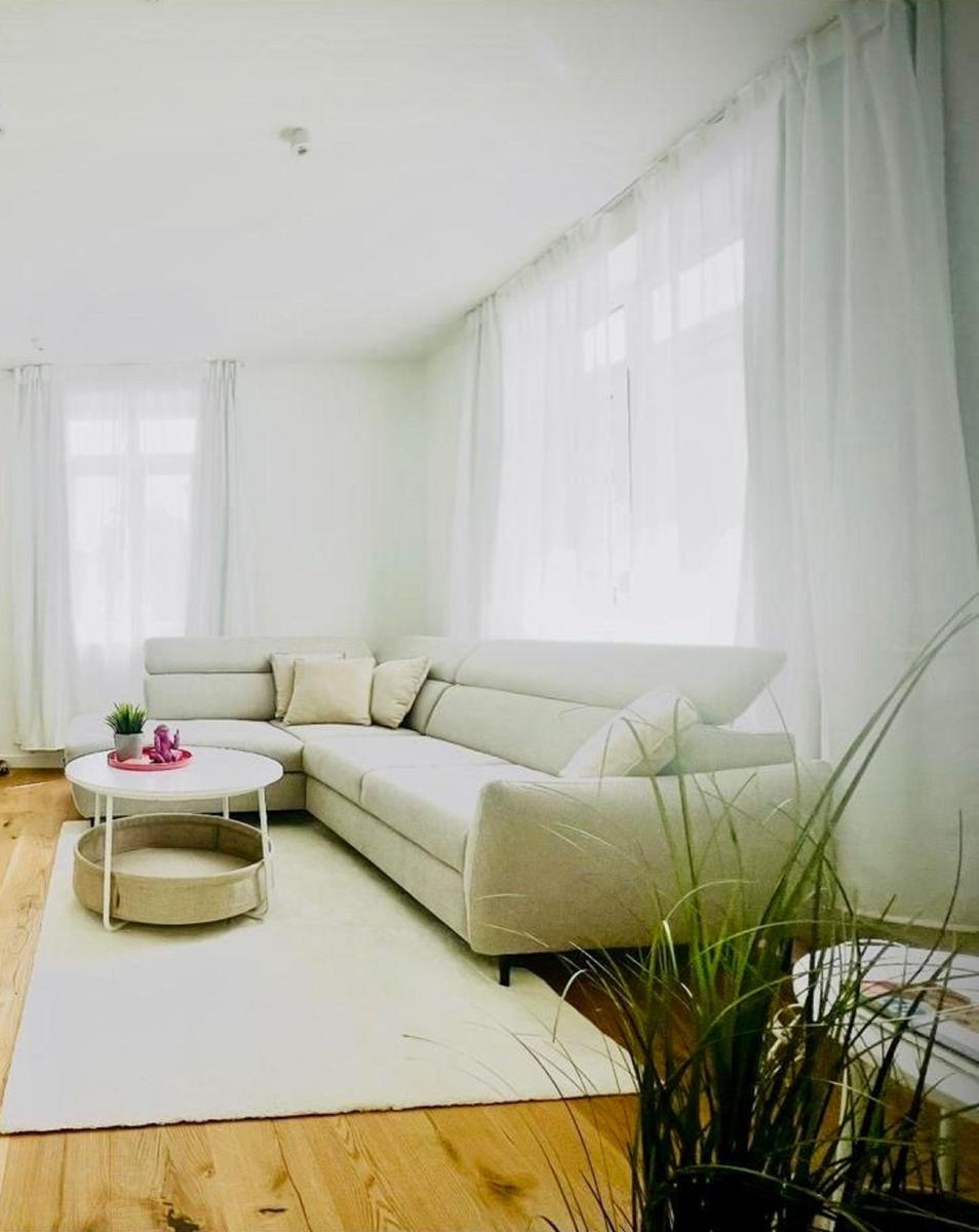 Wohnzimmer mit Ecksofa, weißem Tisch und Pflanzen.