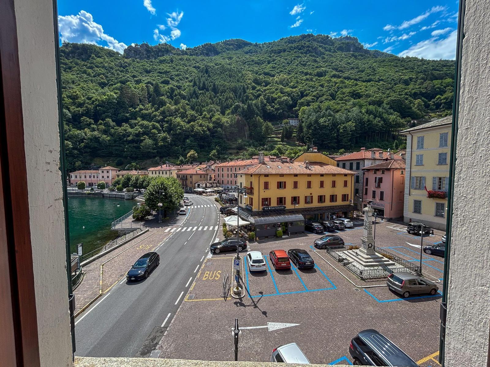View of a square with parking, roads, and a lake in front of green hills.