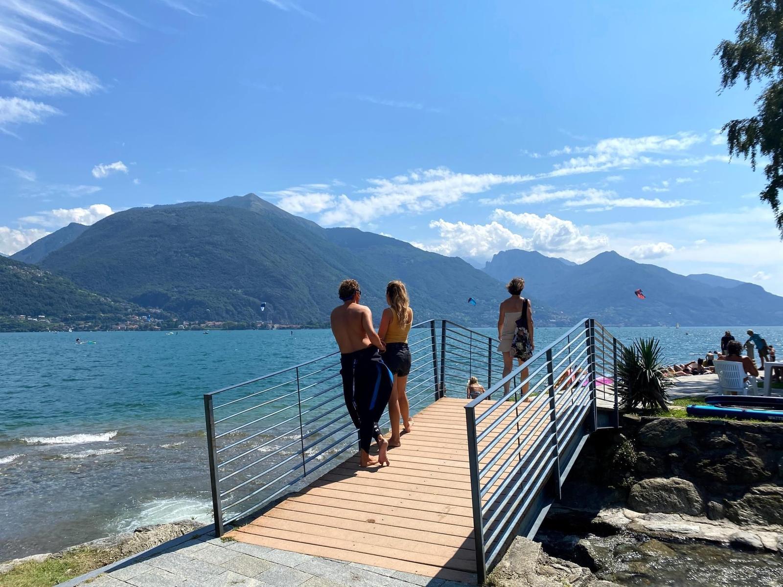 Wooden pier leads to the lake. People enjoy the view of mountains and water.