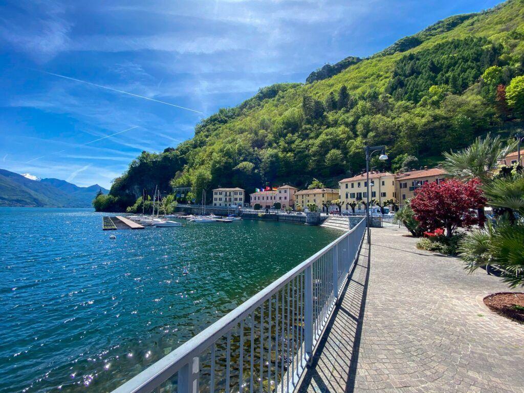 Lakeside promenade with boats and green hills in the background.