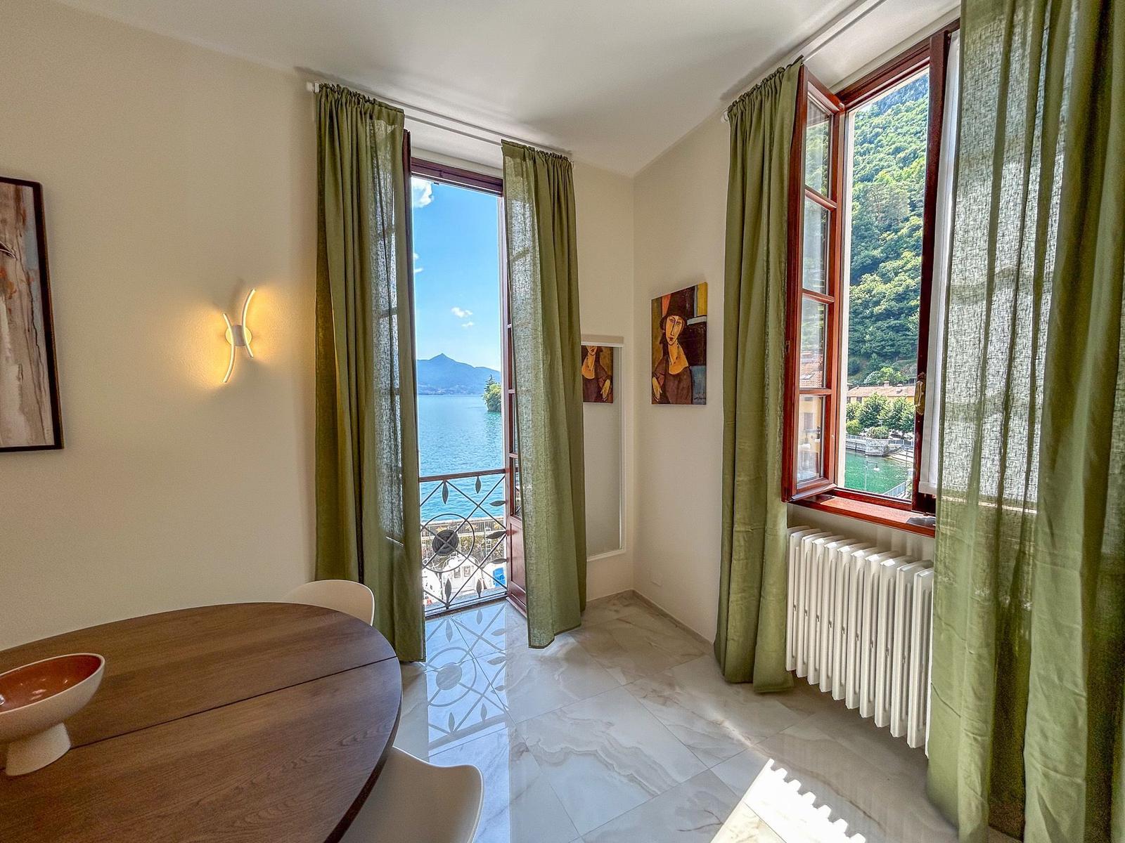 Room with table, windows, and view of lake and mountains.